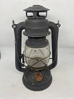 Front view of vintage black metal lantern showing cylindrical glass globe, vented top, side handles, and rust on adjustment knob.