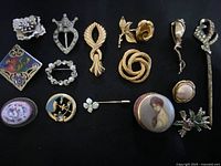 Photo showing collection of assorted vintage brooches and pins on black cloth, approximately measured with ruler in another photo.