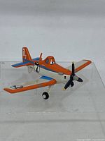 Front angle view of Disney Pixar Dusty diecast aircraft toy showing orange, white and blue paint with propeller and landing gear.