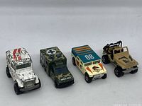 Four Hot Wheels utility vehicles on a white surface, viewed from a front angled side showing detail and wear.
