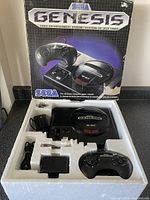 Sega Genesis console in original styrofoam packaging with one controller, power adapter, and cables inside.