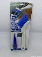 Front side packaging of the Home Essentials sliding door brush with scraper showing the brush with blue bristles and accompanying blue scraper, blister-packed on cardboard.