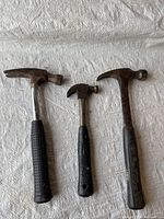Three claw hammers laid on white textured surface, showing front sides and horn claws