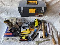 Photo showing entire lot including toolbox, hammer, staple guns, measuring tapes, tapes, sandpaper, and metal square tool