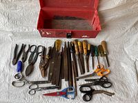 Top-down view showing the red toolbox open and the various tools laid out in front including files, chisels, scissors, screwdrivers and pliers.