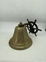 Photo of the vintage brass ship wheel bell showing the bell body and the wheel mounting bracket side angle.