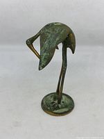 Front diagonal view of the vintage brass crane figurine, showing tarnish and patina developing on surface.
