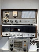 Three vintage CB radios and receivers stacked, showing front controls and meters.