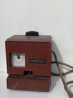 Front view of vintage International time punch clock in red metal with visible clock face and brand plate on front.