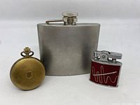 Photo showing all three items: pocket watch, flask, and lighter together for scale and comparison