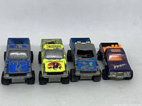 Front and top view of four Majorette Toyota pickup trucks showing varying colors and graphics.