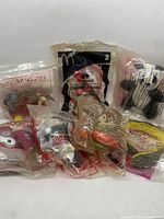 Photo showing multiple McDonald's Happy Meal toys sealed in clear plastic packaging including Looney Tunes characters and others.