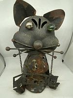Front view showing metal cat sculpture with distinct eyes, facial whiskers, and 'Welcome' sign hanging from chains.