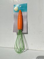 Photo of new whisk with bright orange carrot-shaped handle and green wires on white background, packaged with Wilton brand label.