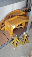 Two yellow 9000lb capacity auto ramps stacked on shelf with two yellow metal jack stands in front, showing general condition and size comparison.