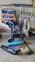 Photo showing the folded colorful striped beach chairs, folded beach cart with blue handle, beach mat, inflatable beach toys, and folded camp table on garage floor.