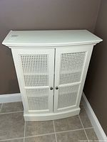 Front view of white bathroom pantry cabinet with dual lattice doors placed against corner wall on tiled floor.