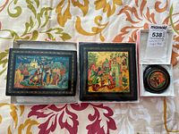 Three Russian lacquered trinket boxes showing detailed hand-painted scenes in vibrant color with gold border, including knights and medieval settings.