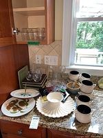 Collection of ceramic soup crocks, plates, glassware, and serving dishes on kitchen countertop.