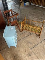Photo of the doll high chair, doll cradle with floral cushion, and doll dresser placed on a wooden floor showing the whole set.