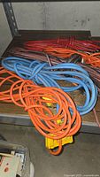 Four large outdoor extension cords coiled on shelving: orange, blue, red, and brownish colors