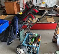 Photo showing Walter Hagen golf clubs in blue golf bag on push caddy with storage basket containing golf balls and two pairs of Footjoy golf shoes on the side.