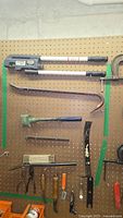Overview of assortment of hand tools and crowbars hung on pegboard, showing various sizes and types including large pipe cutter and crowbars.