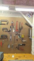 Wide view of pegboard with assortment of hand tools including C-clamps, locking pliers, pipe wrench, adjustable wrench, and other small hand tools hung and arranged neatly.