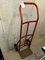 Front view of the red steel hand truck showing handle, frame, wheels, and platform.