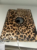Closed leopard print folio cover with Apple logo window and charging cable plugged in