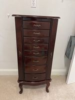 Front view of wooden jewelry chest showing 8 drawers with metal handles and curved legs.