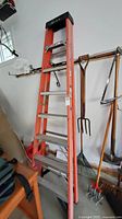 Full view of 8 ft orange fiberglass Werner stepladder leaning against a wall with tools in background