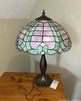 Full view of stained glass style table lamp placed on wooden surface with cord and plug visible.