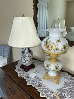 Both lamps on wooden dresser with lace runner, the Asian ceramic lamp with cream shade and the vintage parlor lamp with floral white glass and gold base.