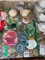 Top-down view showing artisan leaf-shaped bowls in green and red, cream and sugar sets, honey pot, Hungarian terracotta pitcher, and Mikasa dishware neatly arranged.