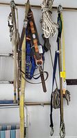 Overall photo showing hanging safety harnesses in blue and tan with ropes and straps attached, all weathered and used.