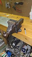 Side angle photo of the heavy metal Reed bench vise mounted on wooden workbench, showing large jaws and round handle.