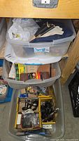 Three stacked clear plastic tubs filled with mixed workshop and safety items seen from above and side
