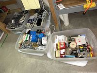 Four large plastic bins containing assorted electrician supplies, including various hardware components and tapes.