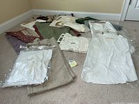 Wide view of the assortment of table linens laid out on the floor showing different fabrics, colors and styles including vintage whites with lace.
