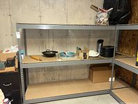 Straight-on view of the full metal utility shelf showing three shelves and some items stored on the middle shelf, which are not included in the sale.