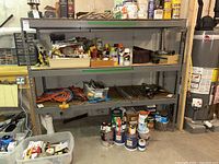Front view of steel shelving unit filled with various paint cans, jars, and other items stored.