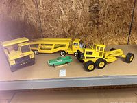 View of three yellow Tonka metal trucks alongside a small green plastic car