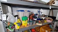 Multiple garden supply items including bags of sunflower seeds, nutrient packets, planters, and tools on metal shelving in a garage.