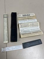 Two vintage slide rules shown with their respective cases and instruction sheet for large one