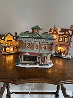 Three ceramic village houses on table, florist shop in front, two other lighted houses behind