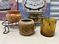 Four flower pots and two metal pot stands arranged on a flat surface with a decorative backdrop.