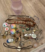Photo of assorted jewelry items spread out on a wooden surface including bead necklaces, bracelets, pins, brooches, rings, and earrings.