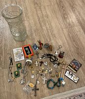 Full view of religious trinkets on wood floor including glass vase, crosses, medallions, figurines, beads, and keychains
