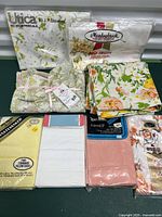 Lot of vintage linens including pillowcases and flat sheets from various brands. Items arranged on dark green surface showing a variety of colors and original packaging.